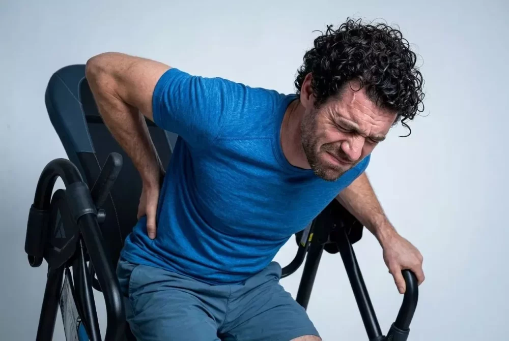 Man with back pain grimacing while holding his lower back on an inversion table.